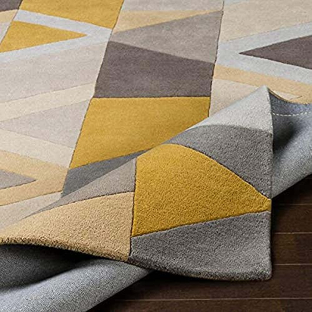 A close-up of a geometric area rug with a folded corner showing the underside, featuring a pattern of mustard yellow, gray, taupe, and beige triangles on a dark wood floor.