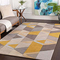 A modern geometric area rug with a patchwork design of mustard yellow, gray, taupe, and cream triangles, shown in a styled living room setting.