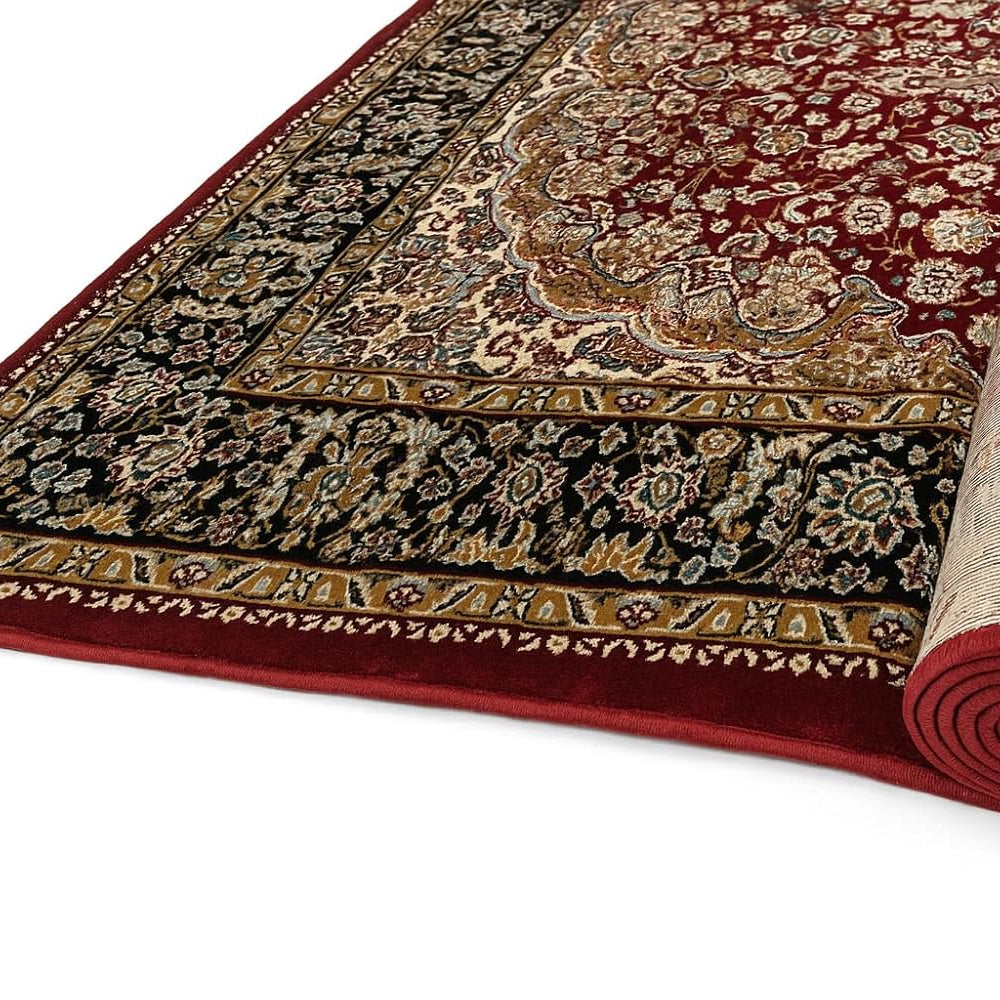 A traditional oriental area rug shown partially unrolled, displaying its deep red field, ornate beige and gold central medallion, and a dark navy outer border with floral motifs.