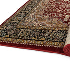 A traditional oriental area rug shown partially unrolled, displaying its deep red field, ornate beige and gold central medallion, and a dark navy outer border with floral motifs.
