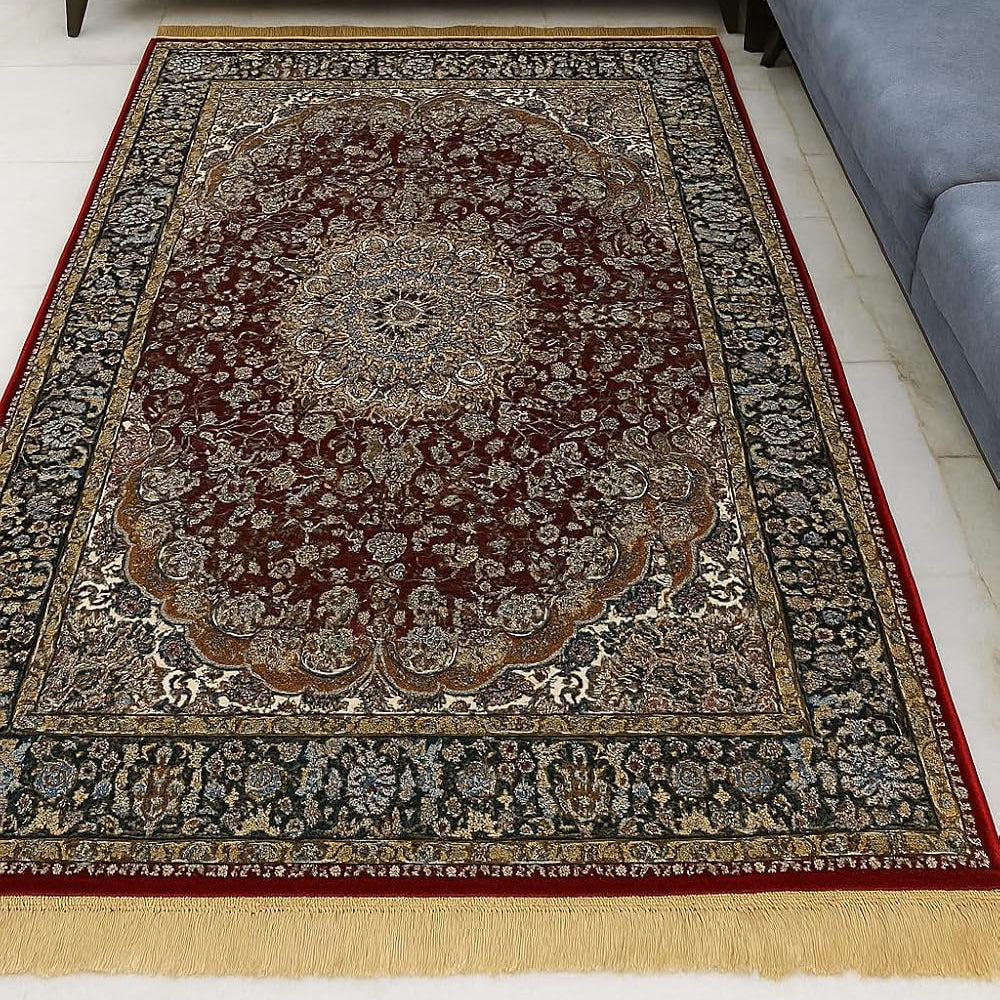 A traditional Persian-style area rug with a dark red central field, intricate floral motifs, and a red border, shown on a white floor in front of a gray sectional sofa.