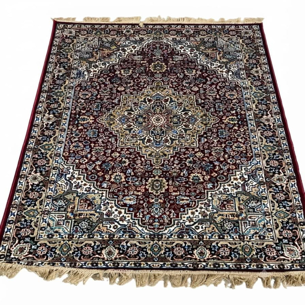 A traditional oriental area rug with an intricate floral and geometric pattern, featuring a dark red central field, beige and blue borders, and cream-colored fringe on the top and bottom edges.