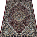 A traditional oriental area rug with an intricate floral and geometric pattern, featuring a dark red central field, beige and blue borders, and cream-colored fringe on the top and bottom edges.