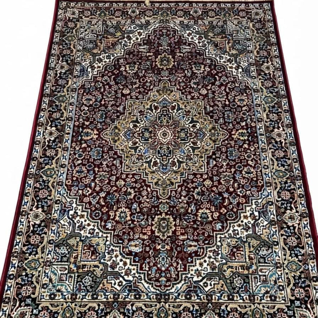A traditional oriental area rug with an intricate floral and geometric pattern, featuring a dark red central field, beige and blue borders, and cream-colored fringe on the top and bottom edges.