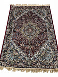 A traditional oriental area rug with an intricate floral and geometric pattern, featuring a dark red central field, beige and blue borders, and cream-colored fringe on the top and bottom edges.