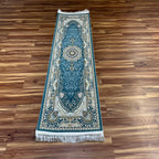 A long rectangular area rug with an ornate traditional pattern in teal blue, cream, and beige, laid out on a polished brown wooden floor.