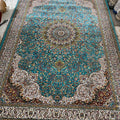 A traditional Persian-style area rug with a vibrant turquoise blue center, intricate floral patterns, and beige fringe, photographed flat on a workshop floor.