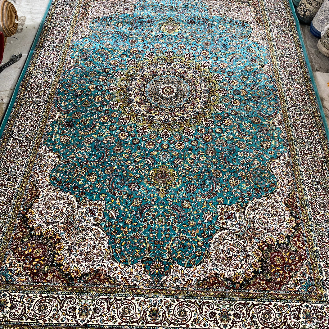 A traditional Persian-style area rug with a vibrant turquoise blue center, intricate floral patterns, and beige fringe, photographed flat on a workshop floor.