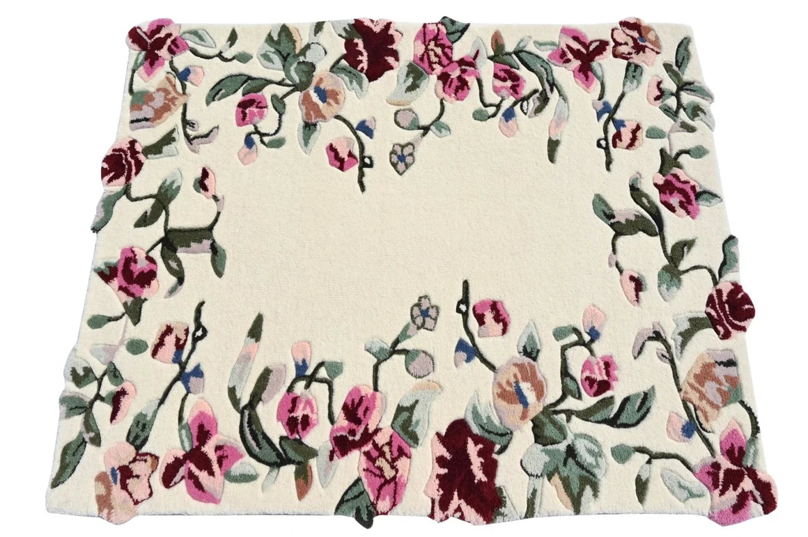 A square cream-colored area rug with a dense floral border pattern featuring pink, burgundy, and green flowers with small blue accents.