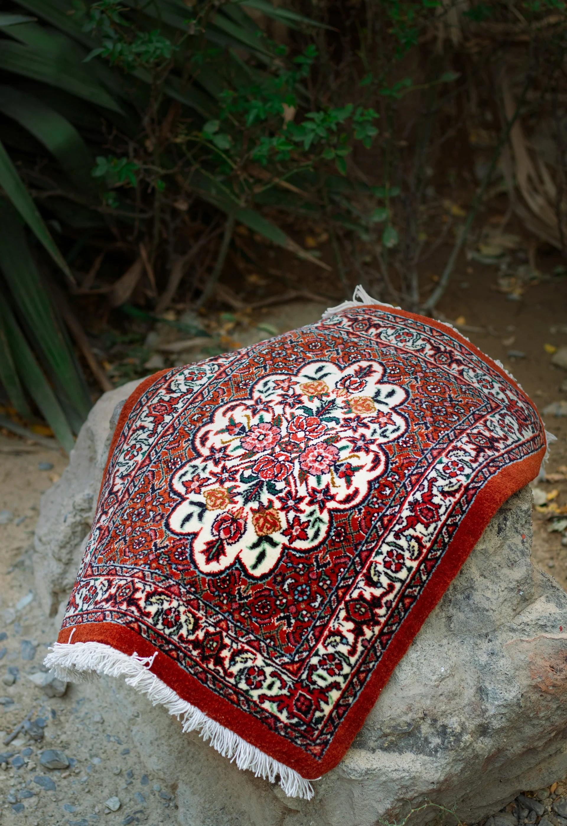 Decorative rug with intricate patterns on a stone surface with greenery in the background
